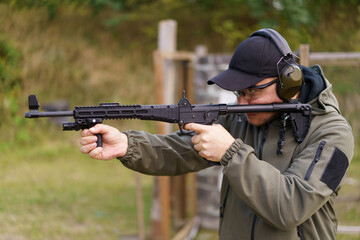 Fototapeta premium A man is holding a gun and wearing a green jacket. He is wearing a black hat and glasses