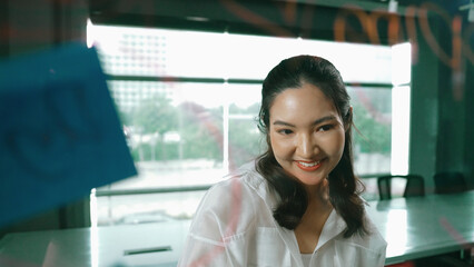 Beautiful female leader thinking about start up project in front of glass board. Smiling young...