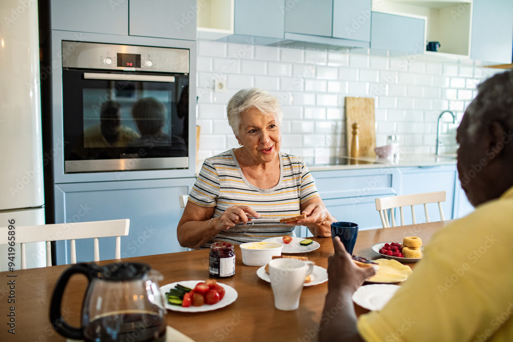 Wall mural diverse senior couple eating breakfast together on the kitchen table