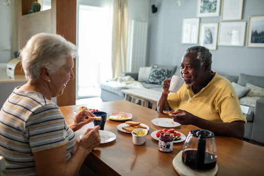 Diverse senior couple eating breakfast together on the kitchen table