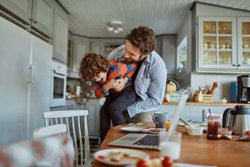 Father and son playing and laughing in kitchen during breakfast