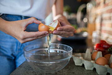 Close-up of women hands cracking an egg into a bowl in the kitchen
