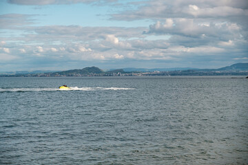 Yellow jet ski glides over calm waters by Edinburgh city skyline