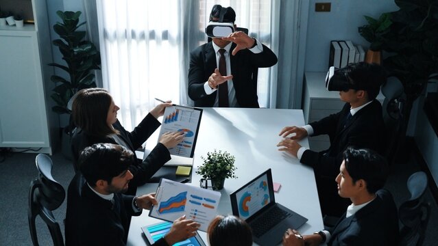 Top view of manager working on laptop and sending data analysis to business people by using VR glass headset while diverse team planning marketing strategy and looking at financial graph. Directorate.
