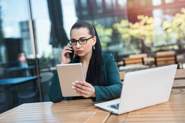 Businesswoman talking by smartphone working with tablet laptop outdoor in cafe. Business concept