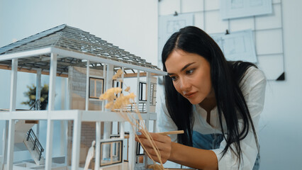 Young beautiful caucasian architect engineer turns house model around to inspect house construction...
