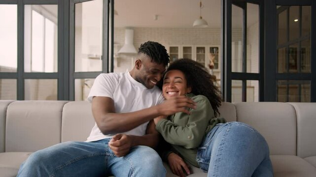 Happy couple African American ethnic family smiling woman man girl guy fall jump on couch jumping own home satisfied husband wife homeowners moving relocation casual weekend cuddle relax on cozy sofa