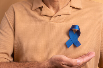hands of mature man showing blue ribbon in studio shot. prostate cancer, awareness concept.