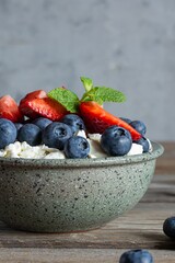 A bowl with cottage cheese, yogurt, fresh berries (blueberries, strawberries) and fresh mint on a wooden background. Delicious breakfast, healthy food.