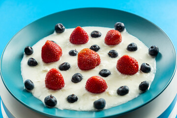 Fresh juicy berries strawberries and blueberries in a blue plate with thick whipped cream