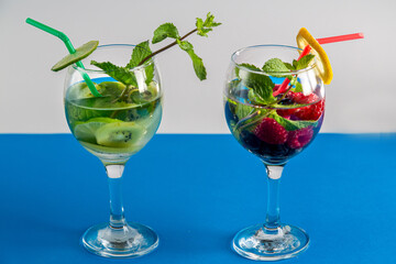 Two Glasses with cocktail kiwi raspberry mint lime with ice on blue background