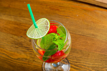 Glass with refreshing cocktail strawberry mint lime with ice on wooden table