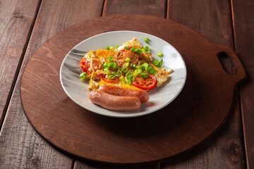 Eggs with tomatoes and fried sausage in a plate on a round wooden stand