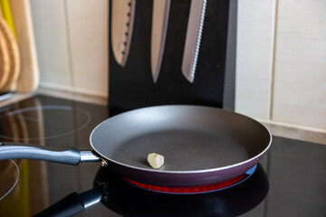 Frying pan with a knob of butter on a  glowing ceramic hob with kitchen knives in the background