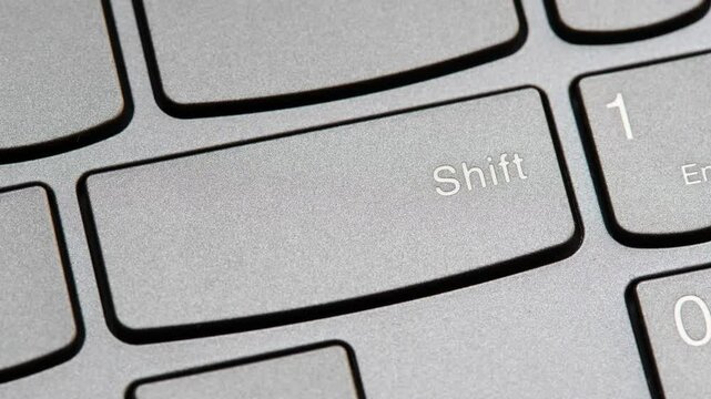 Man pressing the shift key on a modern laptop computer keyboard closeup top view, one person. Shift button key, shifting changing simple abstract concept, capital letters, special characters symbol