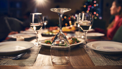 An empty wine glass turned upside down on a dinner table, with a celebratory meal in the background, symbolizing choosing sobriety during social events