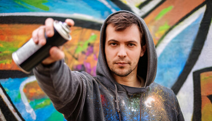 Headshot of a graffiti artist wearing a paint-splattered hoodie, holding a spray can