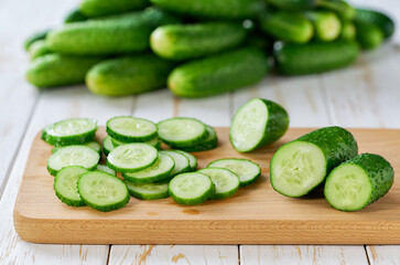 Whole and sliced fresh cucumbers on a cutting board on a wooden table, selective focus.