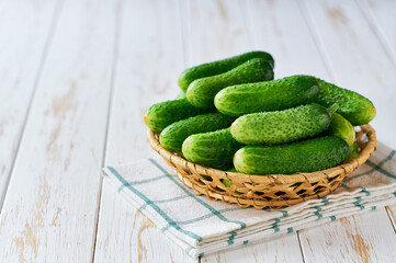 Fresh cucumbers in a basket on light wooden background.