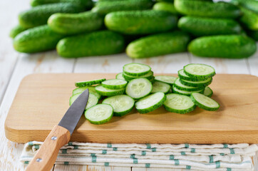 chopped fresh cucumbers slices on a cutting board, on a white kithen table.