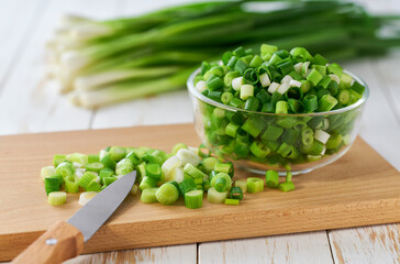 Chopped fresh green onion or scallions in a clear glass bowl , on a white table.