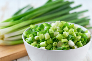 Chopped scallions or young spring onion in a ceramic bowl , on a kitchen table.