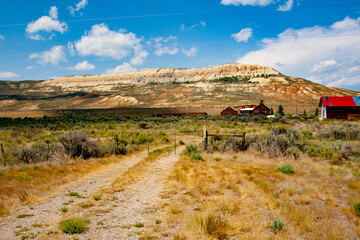 A rugged rural building stands starkly in front of Fossil Butte National Monument, Wyoming, its weathered structure contrasting with the monument's majestic, ancient rock formations.