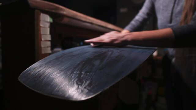 Female hands of a craftsman sanding the sliding surface of a snowboard. Snowboard alignment and repair. Low key. High contrast. Shallow depth of field.