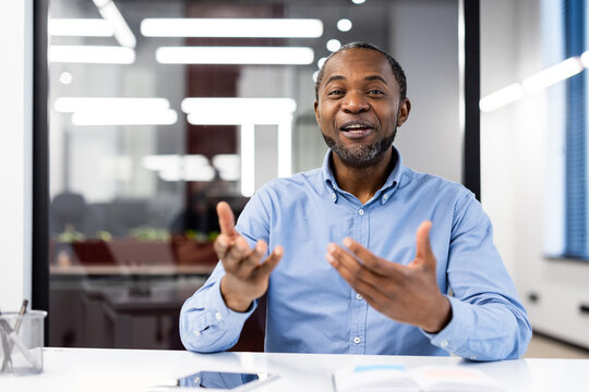 Confident professional man in blue shirt engaging in animated discussion during meeting in modern office. Expressive gestures add dynamism to conversation
