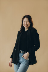 Fototapeta premium A stylish young brunette in a turtleneck and a jacket on a beige background.