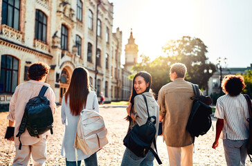  Sincere modern students walk on campus with backpacks to study. Cute confident female student turns to camera and smiles. Education and study at the best university.