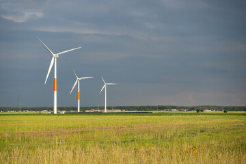 Distant white wind turbines against a dramatic cloudy sky. Meadow in the foreground, taken late afternoon