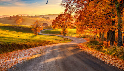 Obraz premium A picturesque country road winding through a hilly landscape, flanked by trees in full autumn colors. The vibrant foliage creates a stunning backdrop