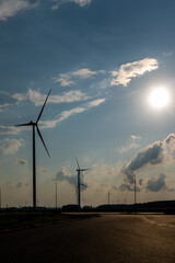 Wind turbines and high voltage electric pylon against blue sky. Sun shining behind the turbines