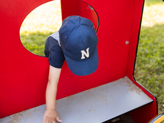 Kind spielt neugierig an rotem Spielgerät im Freien – lebendige Nahaufnahme eines spielerischen...