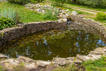 Artificial pond in garden or park. Small pond or lake with stone shore. Landscape design