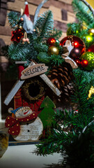 New Year's composition of Christmas tree branches, red, green and yellow balls and other New Year decorations. Wooden house with snowman. Vertical image