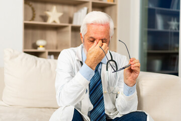 Fototapeta premium Sad tired mature senior male doctor in medical uniform in hospital or doctor office. Unhappy General Practitioner GP therapist professional healthcare expert in clinic. Healthcare concept