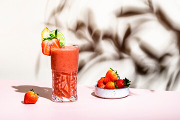 Non-alcoholic mocktail drink with strawberry, banana, syrup, peach juice, lemon and ice in glass. Beige pink background, hard light