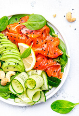 Keto salad with salmon, avocado, spinach, cucumber, sesame seeds  and cashew nuts.. White background, top view