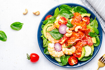 Seafood salad with shrimp, salmon, avocado, spinach, cucumber, tomato, cashew and sesame seeds.. White background, top view