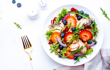 Strawberry and chicken fresh salad with arugula, blueberries, onion and walnuts, white background, top view