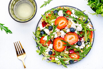 Strawberry and feta salad with arugula, lettuce, blueberries, cheese and walnuts, white background, top view
