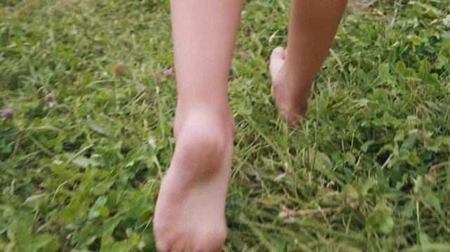 A child walks barefoot through soft, vibrant grass, exploring the joys of nature. The close-up shot captures the essence of carefree summer days.