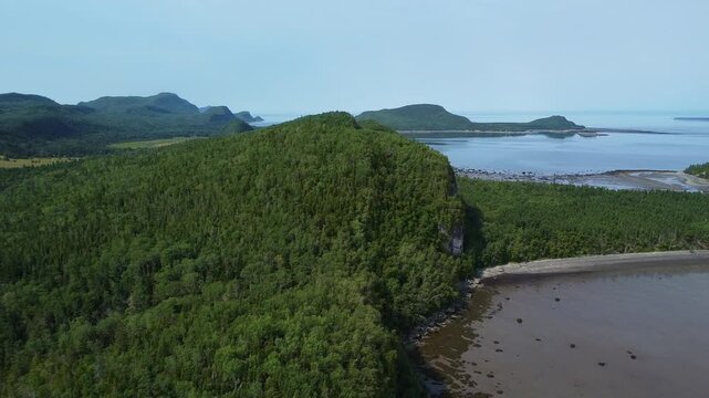 Survol de drone au-dessus de montagnes luxuriantes ,de caps rocheux et de plages sablonneuses  bordant le bord du Fleuve Saint-Laurent sous un ciel bleu sans nuages. Parc du Bic, Qu&eacute;bec, Canada.