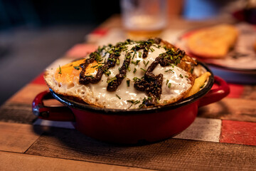 Patatas bravas with a sunny side up egg and truffle sauce in an enameled pot