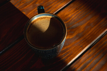 coffee in a mug close-up with foam on a wooden table, background, morning light rays, contrast, top...