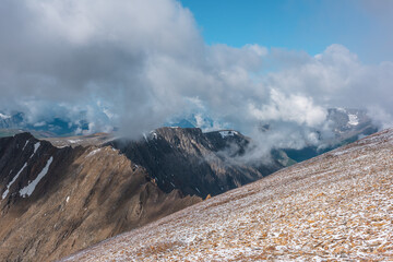 Scenic view from snowy stony hill to sharp ridge separating two alpine valleys and snow-white...