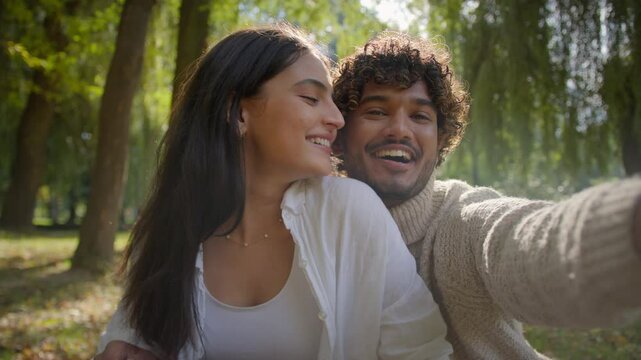 Carefree multiracial couple Arabic Indian male boyfriend happy Hispanic girlfriend woman making photo on mobile phone device outside in park man female laugh smile filming video cuddle honeymoon love