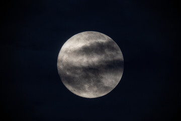 photograph of the full moon partially covered with clouds
